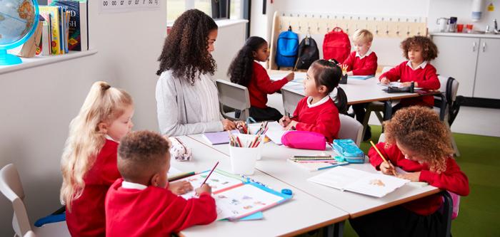 Reception teacher sitting on a table with school children